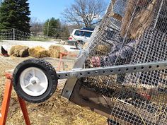 a chicken in a cage with wheels attached to it's sides and hay on the ground