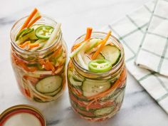 two mason jars filled with pickles, cucumbers and carrots sitting on a table