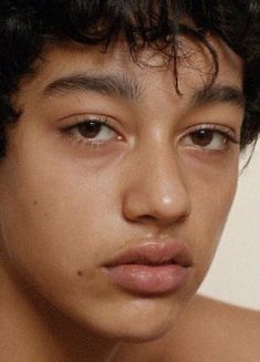 a close up of a young man with curly hair and no shirt looking at the camera