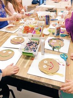 a group of children sitting at a table making crafts with paper plates and scissors on it