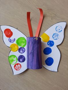 a butterfly made out of toilet paper and colored buttons on it's wings, sitting on a table