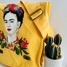 Be inspired by the vibrant Frida with this limited edition shoulder or crossbody messenger bag! Featuring a beautiful portrait of the bold Mexican artist among exotic and daring flowers, this bag is both elegant and practical. Perfect for Frida lovers, this is a must-have gift that will surely be cherished. Show off your love for Frida Kahlo, the most iconic artist in Mexico, with this vivid pinkish-red canvas bag. Don't miss out on this unique and useful addition to your collection! Bag Details: • Style: Shoulder/Cross-Body Strap Bag• Bag Color: Washed Yellow mustard/Dainty Lion color shade.• 14 oz 100% Cotton Soft Canvas Fabric• Pigment - Dyed - Heavy Enzyme-washed• Adjustable Cotton Webbing Strap• Front Flap with Antique Brass Metallic Turn-Buckles• Single Large Compartment with Inside Artsy Shoulder Bag Gift, Bohemian Orange Embroidered Bag, Yellow Embroidered Tote Bag, Multicolor Embroidered Crossbody Bag, Artistic Hand Painted Crossbody Shoulder Bag, Frida Kahlo Earrings, Artistic Yellow Tote Bag, Yellow Mustard, Mexican Artists