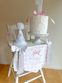 a birthday cake sitting on top of a wooden table next to a white chair with a pink bow