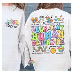 "Dear Tiny Human Behind Me Shirt, Teacher Shirt, Custom Teacher Name, Kindergarten Teacher, Back To School Shirt, Teacher Appreciation Gift ↓ Click here to view our additional fashionable collections ↓ https://handcraftedbyhelenn.etsy.com Product Details: - 100% Cotton (fiber content may vary for different colors) - Medium fabric (5.3 oz/yd2 (180 g/m2)) - Classic fit - Tear away label - Runs true to size Care instructions: - Machine wash: warm (max 40C or 105F); - Non-chlorine: bleach as needed; - Tumble dry: Medium - Do not iron; Do not dry clean ● Please choose your preferred style, size, and color from the dropdown menu or leave us a message in the \"notes to seller\" section. ● We are committed to processing and shipping your items as quickly as possible, but please note that custom pr Cute Long Sleeve Shirt With Text Print, Fun Long Sleeve T-shirt With Name Print, Multicolor Long Sleeve Shirt With Letter Print, Cute Long Sleeve Tops With Funny Text, Teacher Back To School, Kindergarten Teacher, Teacher Name, Teacher Appreciation Gift, Kindergarten Teachers