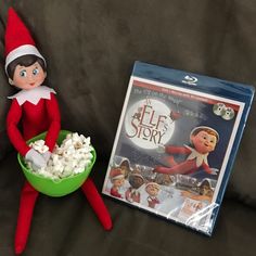 an elf is sitting on the couch next to a bowl of popcorn and a dvd