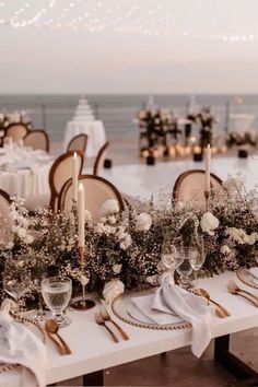 a table set up with white flowers and candles for an elegant dinner by the ocean