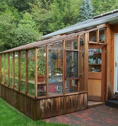 a small wooden greenhouse with lots of plants in the room and shelves on the wall