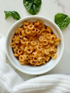 a white bowl filled with macaroni and cheese on top of a table next to basil leaves