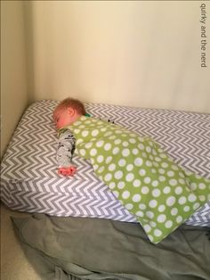 a baby laying on top of a bed next to a green and white coverlet