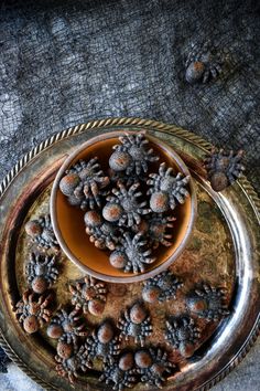 a bowl filled with liquid sitting on top of a metal tray covered in pine cones