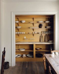 an open cabinet with plates and glasses on it in a room that has wooden floors