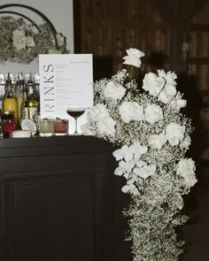 a bar with white flowers and wine glasses on the top shelf in front of it