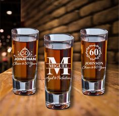 three shot glasses sitting on top of a wooden table with the names of two people