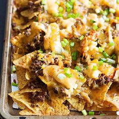 a tray filled with nachos topped with cheese and green onions