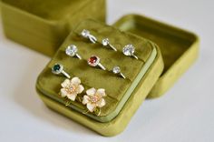 an assortment of rings sitting in a green case on top of a white tablecloth