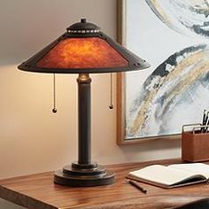 a desk lamp sitting on top of a wooden table next to a book and pen