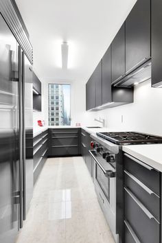 a long kitchen with stainless steel appliances and white counter tops, along with marble flooring