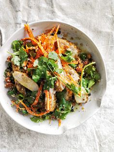 a white bowl filled with lots of food on top of a tablecloth next to utensils