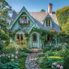 a green house surrounded by flowers and greenery in the front yard, with stone pathway leading to it