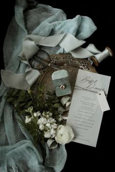 a table topped with flowers and jewelry on top of a blue cloth next to a silver tray