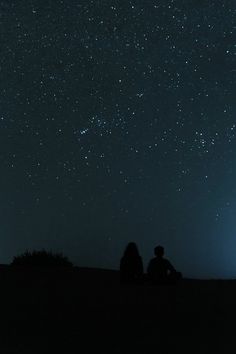 two people are sitting under the stars in the sky