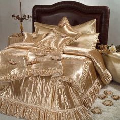 a bed with gold sheets and pillows in a room next to a vase filled with flowers