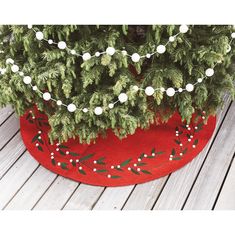 a christmas tree skirt with holly and white balls on it, sitting on a wooden deck