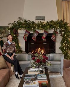 a woman sitting on a couch in front of a fire place filled with christmas decorations