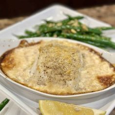 a white plate topped with a dish of food next to green beans and lemon wedges