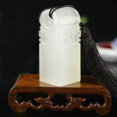 a white vase sitting on top of a wooden stand next to a black tassel