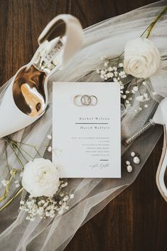 two wedding rings on top of a white piece of paper next to flowers and shoes