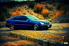 a blue car parked on the side of a road next to a hill and grass