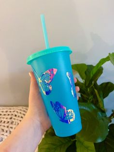 a person holding a blue cup with butterflies on it and a green straw in their hand