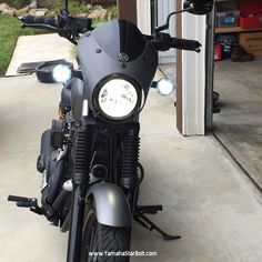 a black motorcycle parked in front of a building with lights on it's headlight