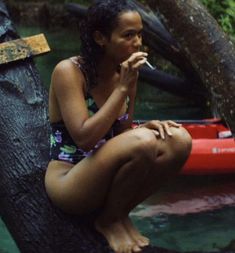 a woman sitting on top of a tree next to a red raft in the water