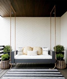 a porch swing with pillows and plants on it