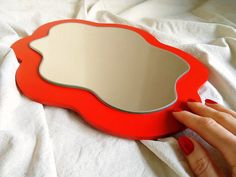 a woman's hand holding a red mirror on top of a white sheet