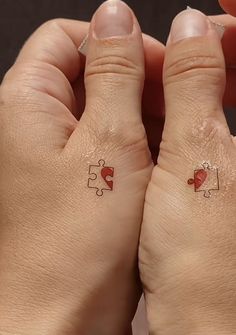 two hands with matching tattoos holding each other's heart and puzzle pieces on their fingers