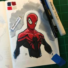 a drawing of spider - man on paper with markers and marker pens next to it