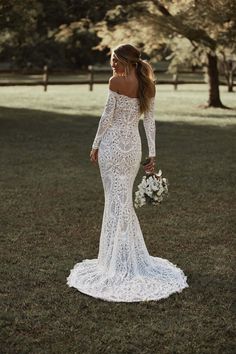 a woman in a white wedding dress standing on grass with her back to the camera