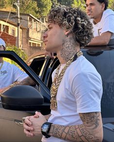 two men sitting in the back of a car, one with tattoos on his arm