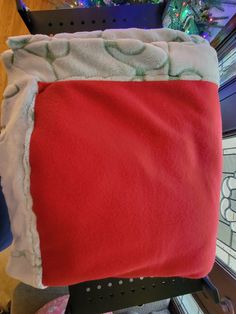 a red and white blanket sitting on top of a black chair next to a christmas tree