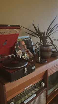 an old record player sitting on top of a table next to a potted plant