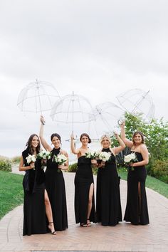 four bridesmaids holding umbrellas in their hands and posing for the camera on a brick walkway