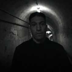 a man standing in a dark tunnel with his head turned to the side and looking at the camera