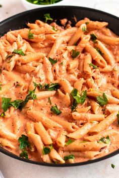 a skillet filled with pasta and sauce on top of a white tablecloth next to some parsley