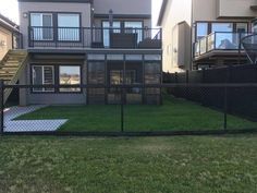 a fenced in yard with grass and stairs leading up to the back of two story houses