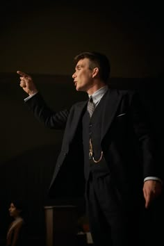 a man in a suit and tie standing up with his hand out to the side