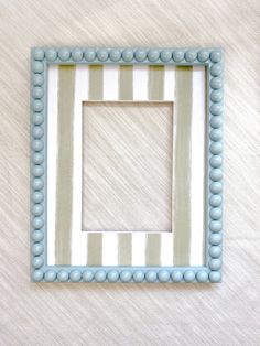 a blue and white striped frame with beads on the edges is hanging on a wall