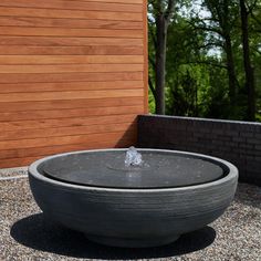 a water fountain in the middle of a graveled area next to a wooden wall